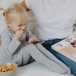 A mother and daughter enjoying storytime on a cozy couch with snacks nearby.