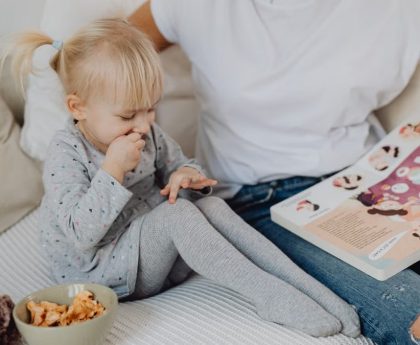 A mother and daughter enjoying storytime on a cozy couch with snacks nearby.