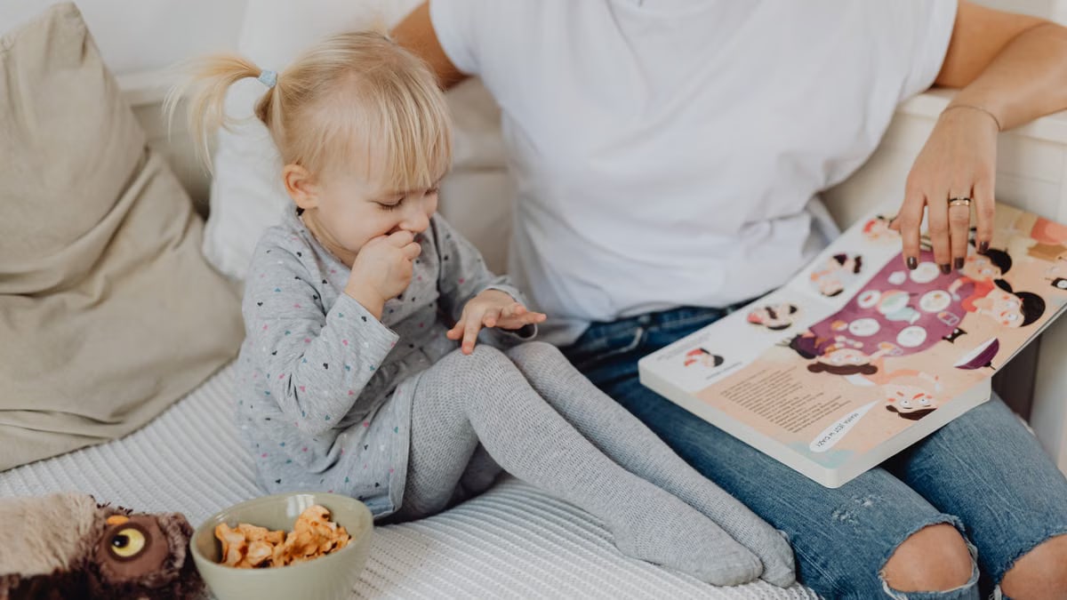 A mother and daughter enjoying storytime on a cozy couch with snacks nearby.