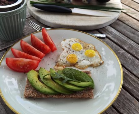 A vibrant outdoor breakfast setup with avocado toast, quail eggs, tomatoes, and tea.